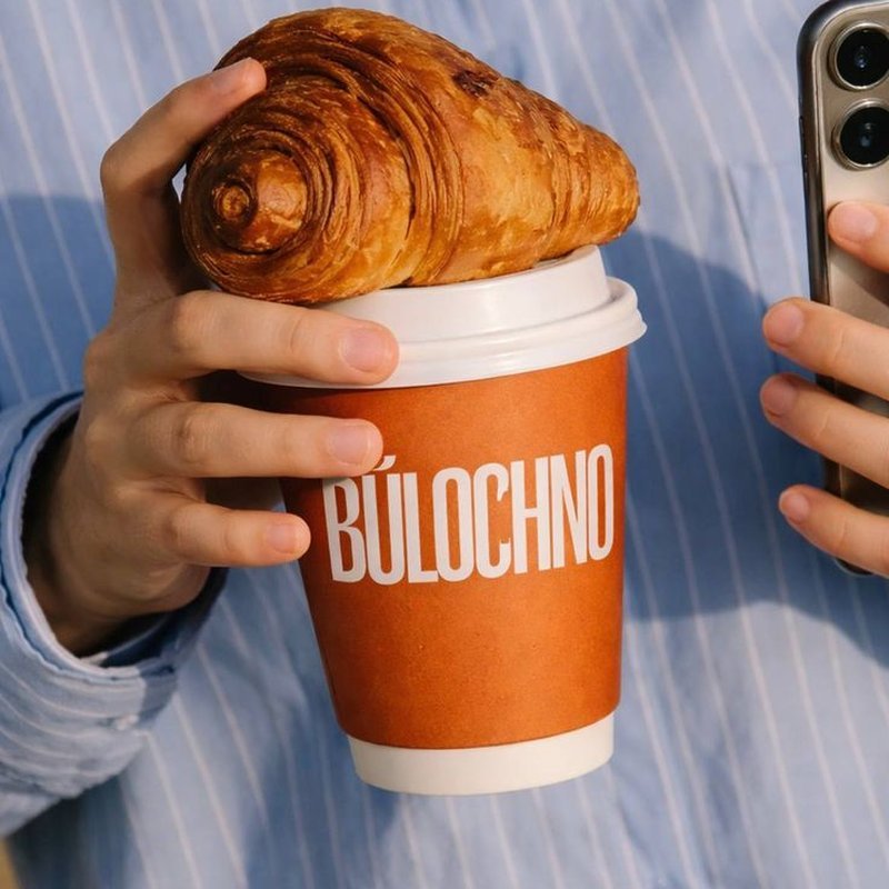 A custom-printed coffee cup held with a croissant